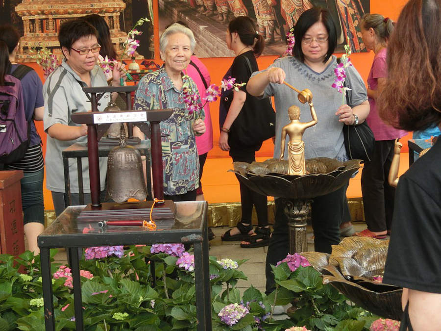 people pour water over buddha statue and give flower offerings