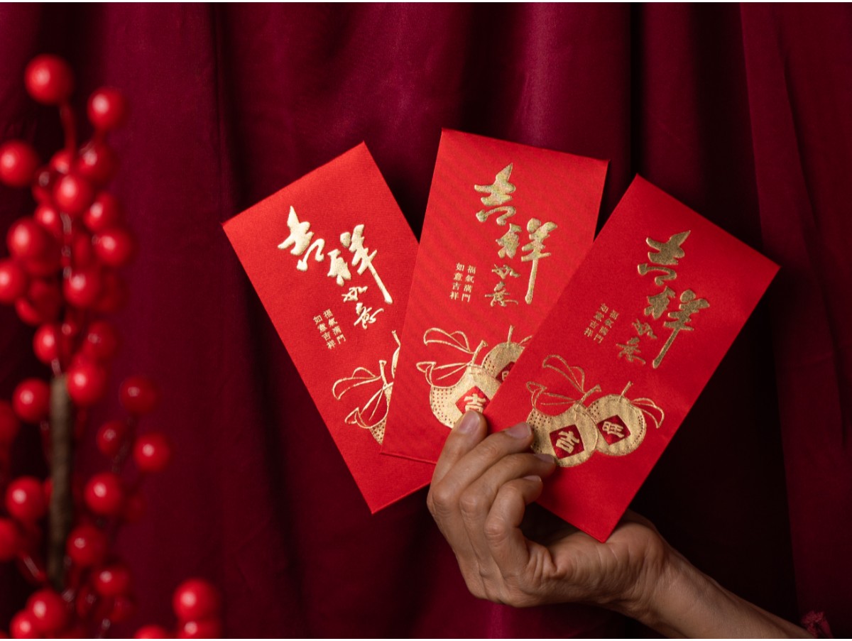 hand holding fanned out lunar new year red envelopes filled with money