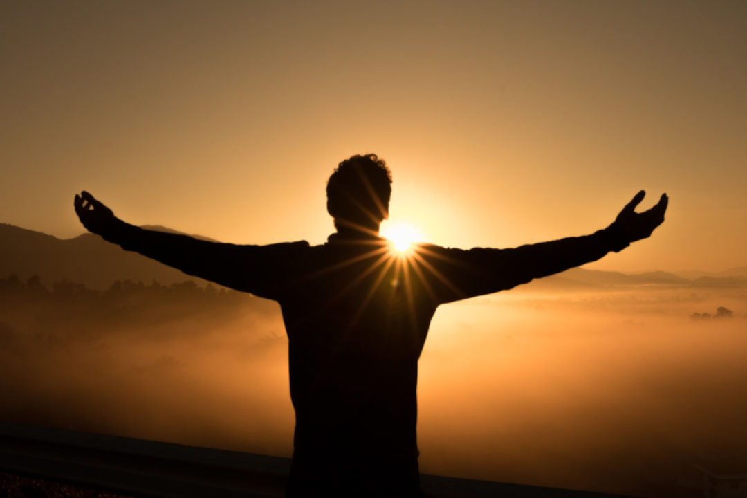 silhouette of person holding out arms to sunrise