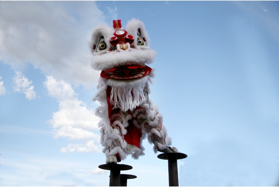 white costumed performer climbing poles in high pole lion dance show
