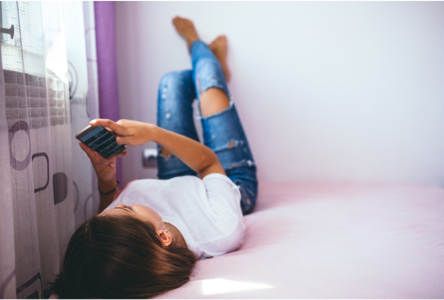 teenager using smartphone while lying on bed