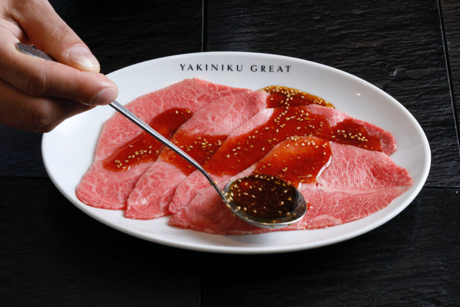 sauce being poured on raw beef slices at yakiniku great