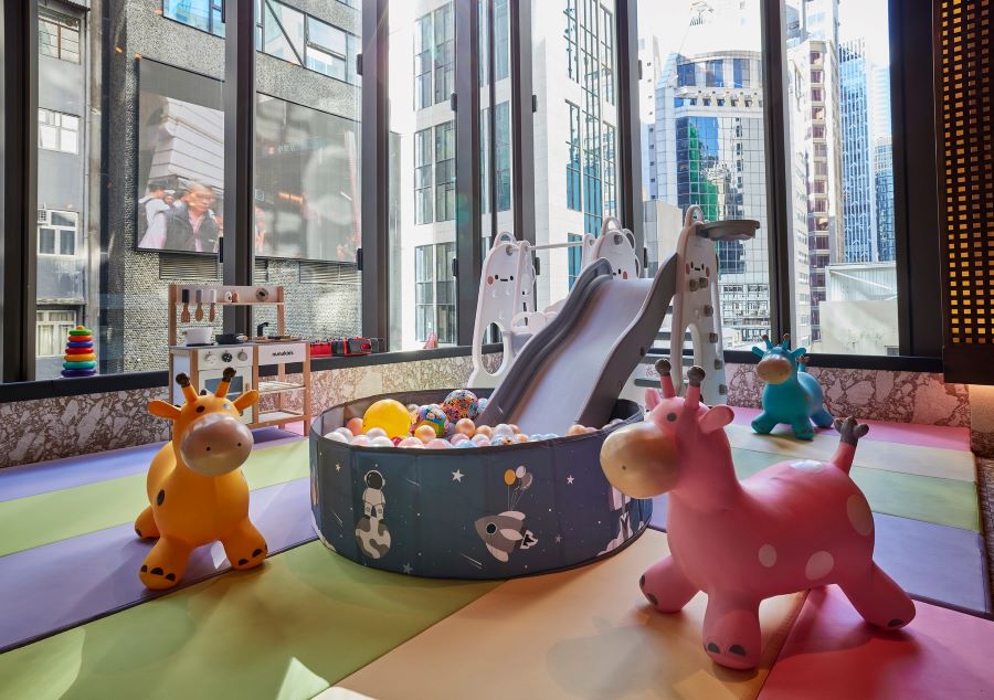The play area at Ministry of Mussels. In the foreground, there are two plastic bouncy cows placed on either side of a slide-cum-ball pit, which also has a swing and a hoop. There are stacking rings and a kitchen station on the left.