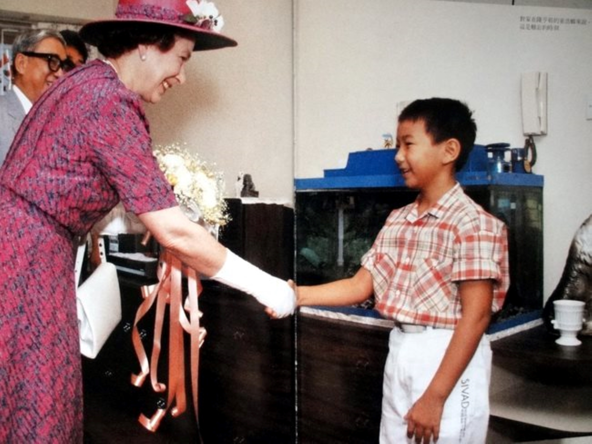 Queen Elizabeth II visiting a Hong Kong family during her visit to the city in 1986. The Queen is on the left, and shaking the hand of a little boy.