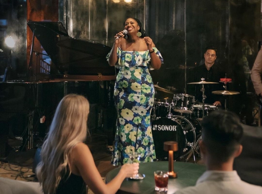 A jazz singer sings for diners at DarkSide in front of a piano and a drummer.