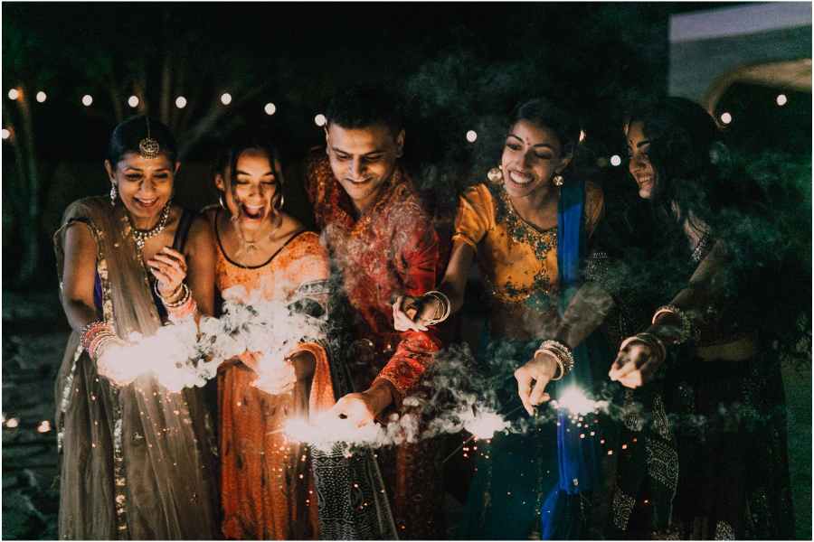 People wearing traditional Indian outfits holding sparklers and celebrating Diwali at night.