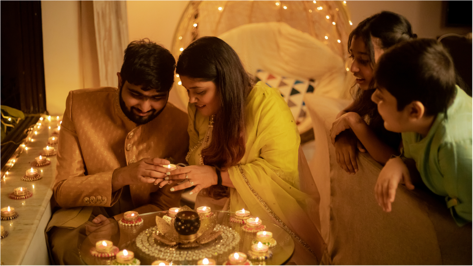 A family of four celebrating Diwali by lighting diyas.