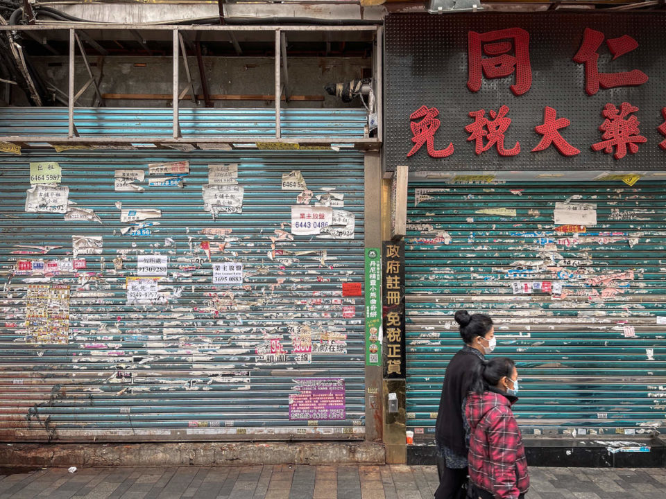 pedestrians wearing mask outside a shuttered shop in hong kong