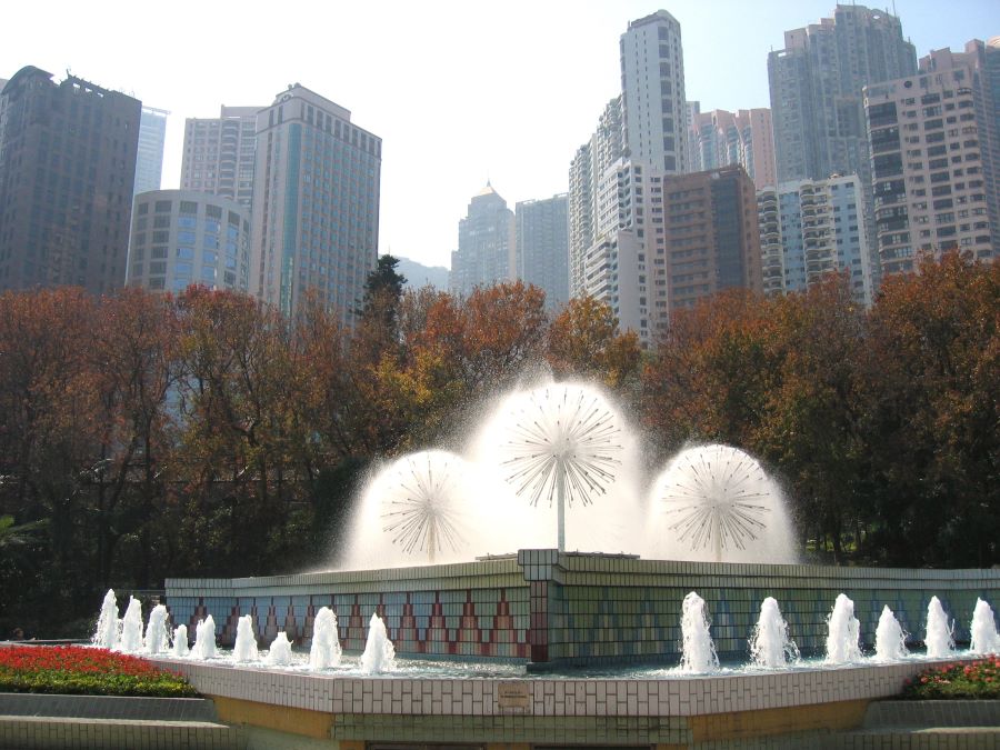 Autumn leaves on trees between the fountain at the Hong Kong Zoological and Botanical Gardens and the city skyline.