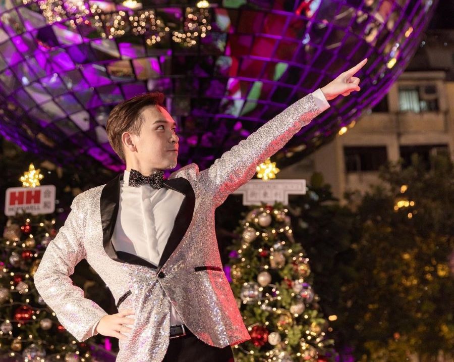 A man in a glittery suit strikes a Saturday Night Fever pose in front of the large disco ball and Christmas trees at Lee Tung Avenue.