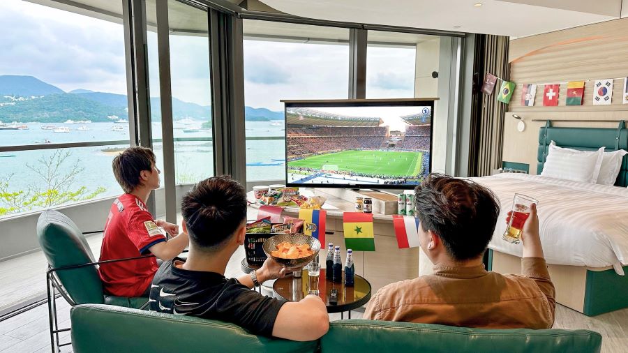 A family watches a football match in a room at the WM Hotel. They have snacks in front of them and the room is decorated with flags that represent the various countries participating in the tournament.
