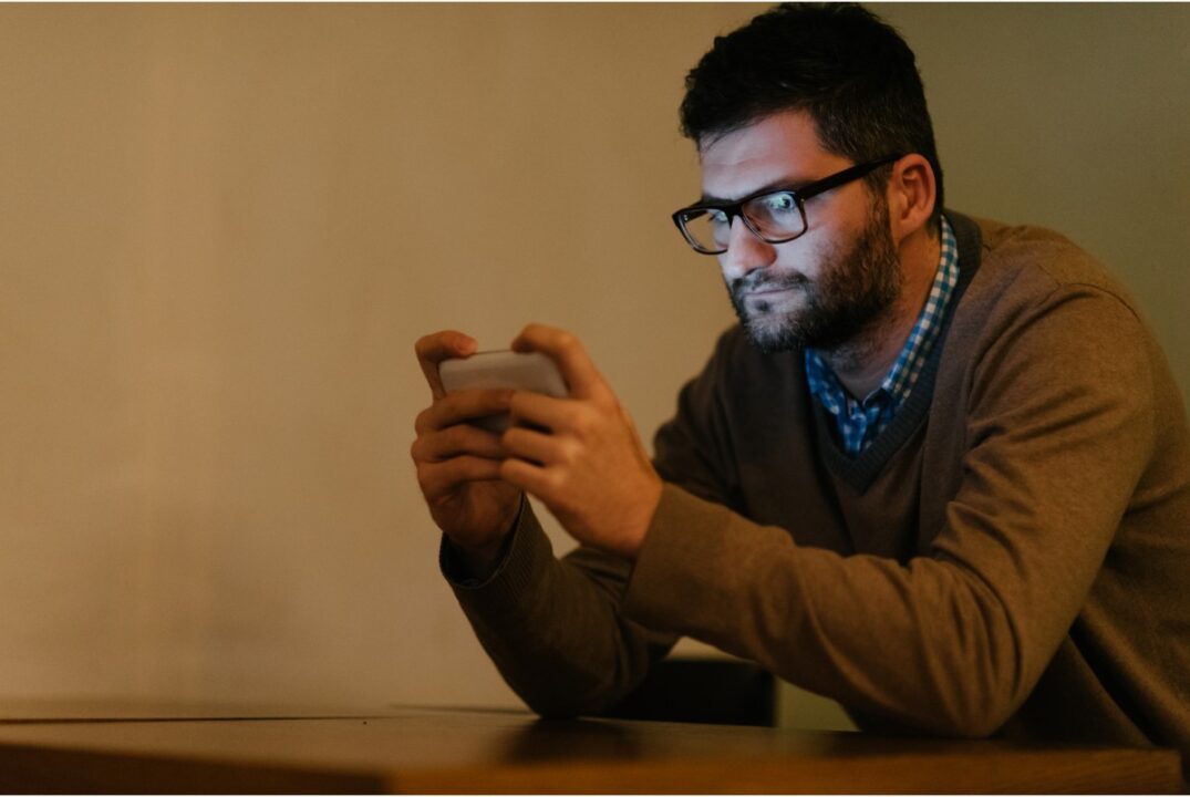 man using phone with blue light reflecting on his face
