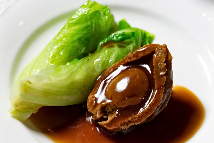 a braised abalone with brown sauce and some Chinese lettuce on the side