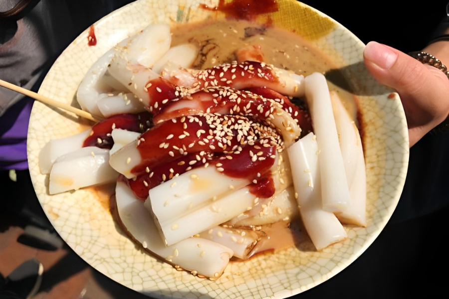 holding a plate of rice rolls with sweet sauce, sesame sauce and soy sauce, with a drizzle of sesame on top