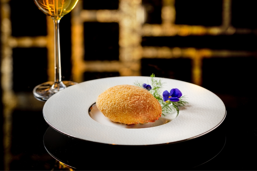 deep-fried stuffed crab shell with edible flower on a plate and a glass of wine on the side