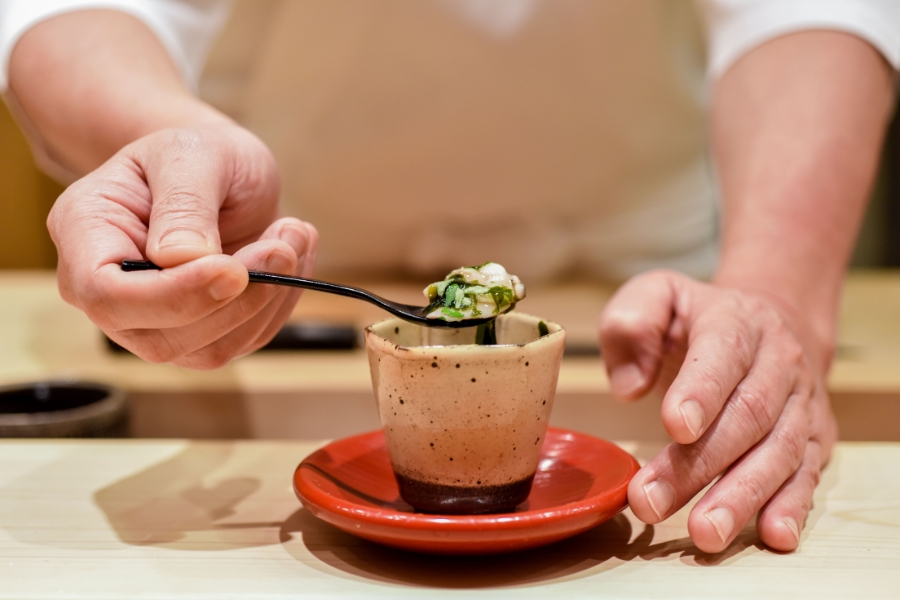 chef is using a spoon is pull the fresh food from a small beige and black cup served on top of a red plate