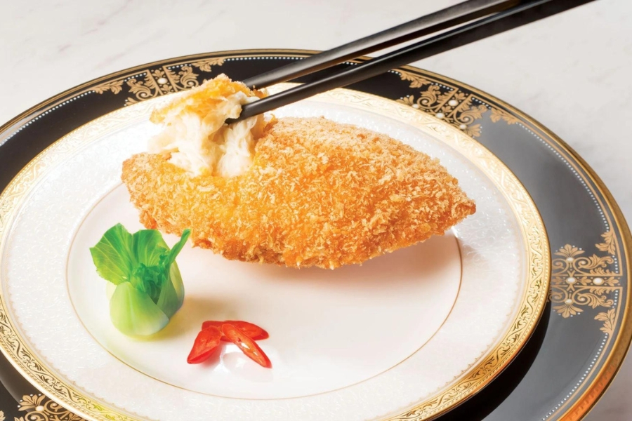 a pair of chopsticks pulling the meat of baked stuffed crab shell served on a black and gold decorative plate