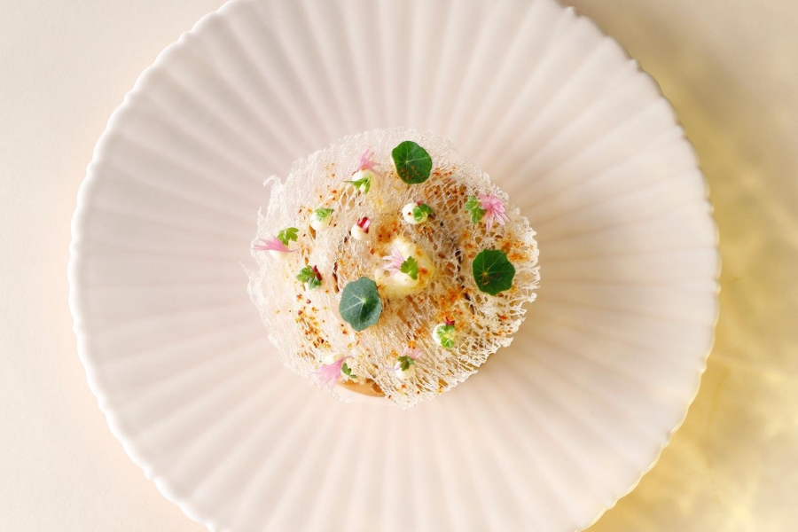 scallop served in a white decorative plate, with a web on top and edible flowers and leaves as decor