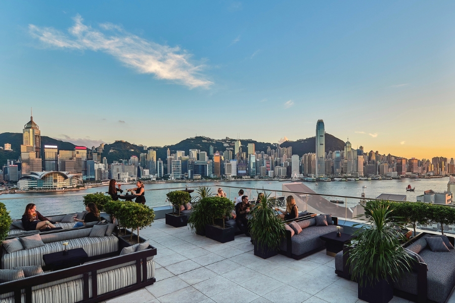 a rooftop terrace with sofa seats overlooking Victoria Harbour during sunset