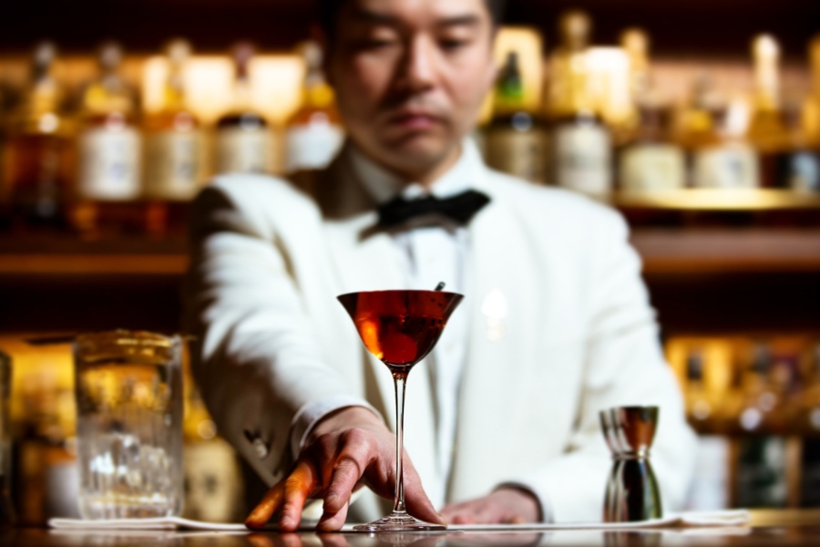 The bartender is dressed in perfect white suit and bow tie while serving a carefully prepared glass of cocktail at Mizunara: The Library