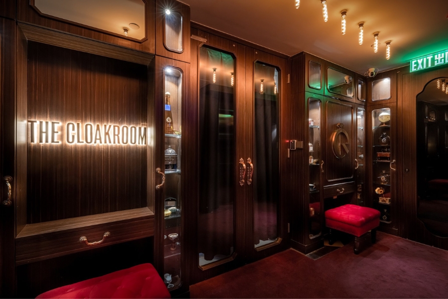 The entrance of The Cloakroom that's mimicking a cloakroom from the 1920s with red wood finishes and red velvet ottomans.