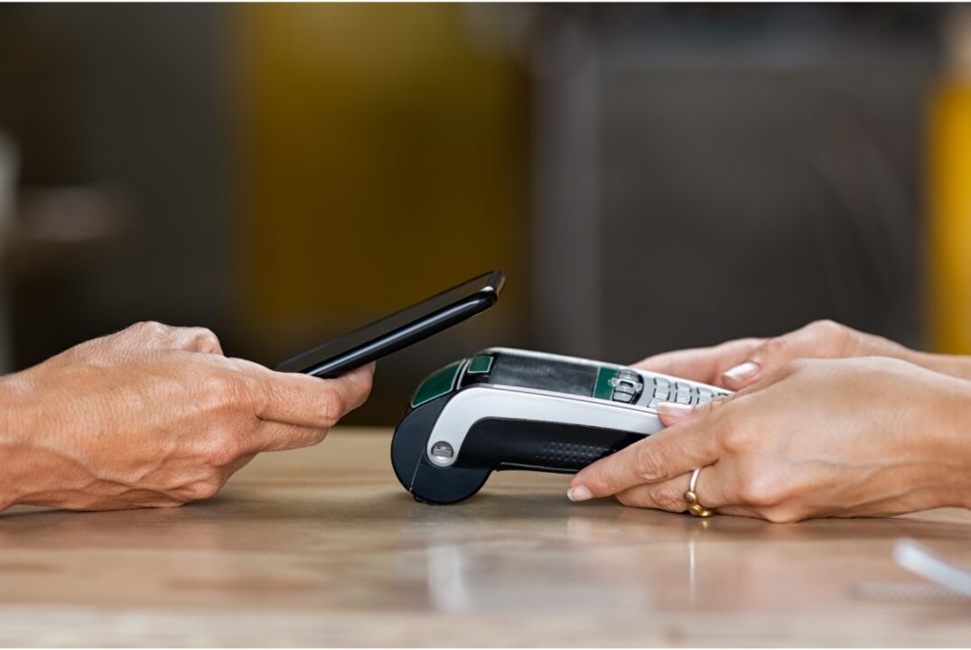 A person making a contactless payment on a credit card reader using a mobile phone.