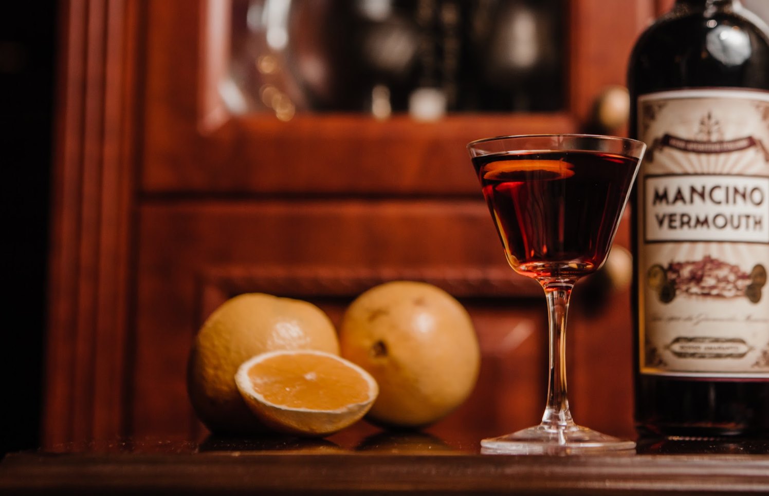 A whiskey cocktail along with fruit and a vermouth set against the wooden interiors of The Wise King.