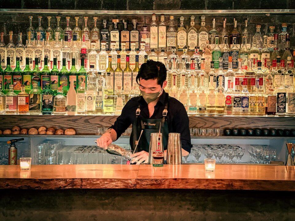 A bartender at Coa mixes a drink in front of shelves lined with several bottles of alcohol.