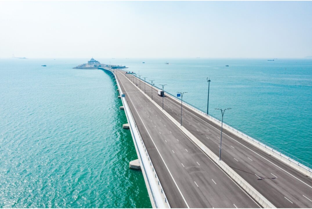 An aerial shot of the Hong Kong-Zhuhai-Macao bridge. There are six lanes flanked by the sea, which lead to the entrance of the undersea tunnel.