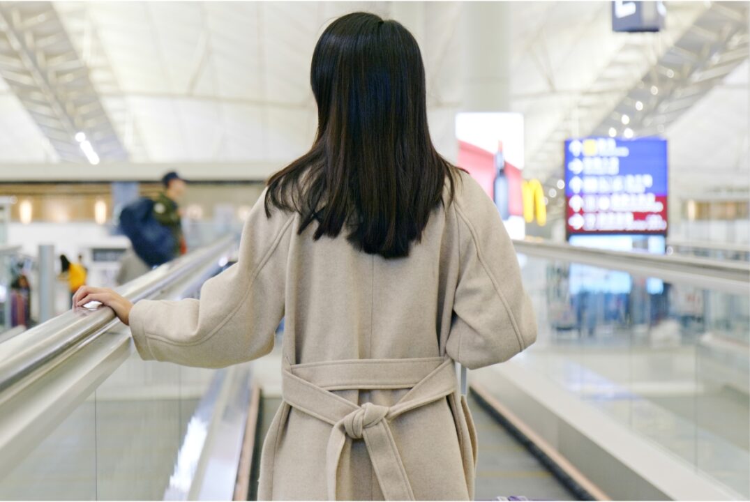 woman wearing a beige jacket at the hong kong international airport. she is on a travelator heading to her boarding gate.
