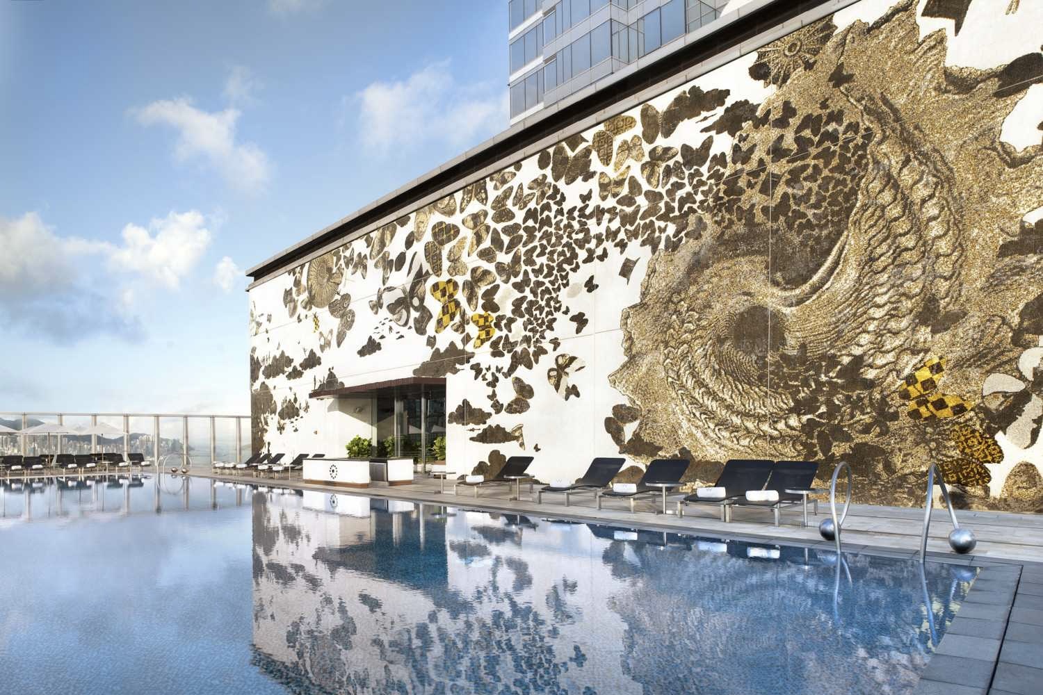 A partial view of the swimming pool of the W Hong Kong, which is lined with deck chairs and overlooks Victoria Harbour. A stunning nature-inspired mural adorns the wall of the building leading into the fitness centre.