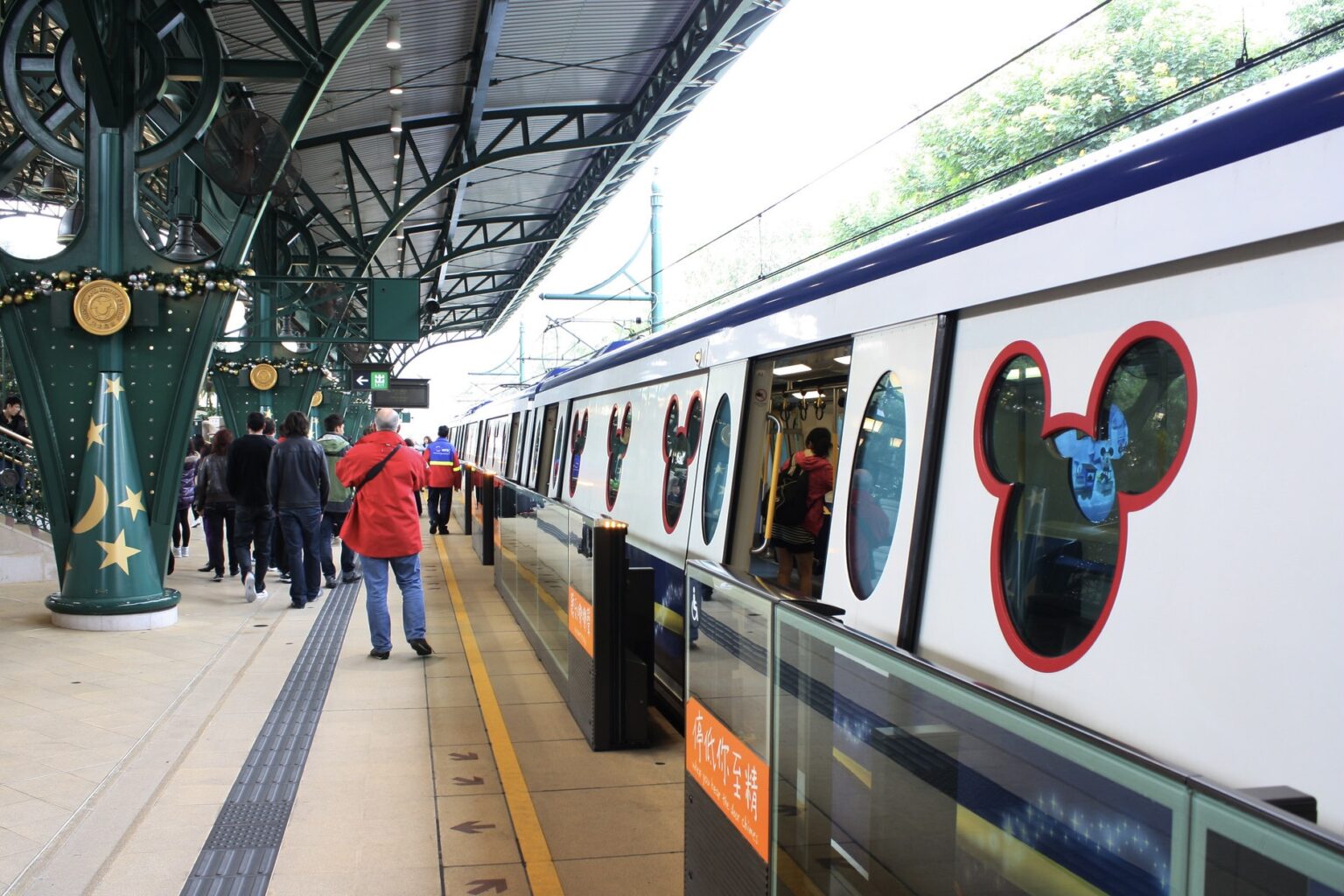 The MTR train at the Disneyland Resort station in Hong Kong. On the right is the train with Mickey Mouse-shaped windows. On the left is the platform with people in front of the train.