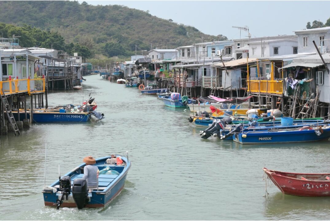 A motorboat sailing the river in Tai O. There are stilt houses on both river banks, and boats moored in front of them.