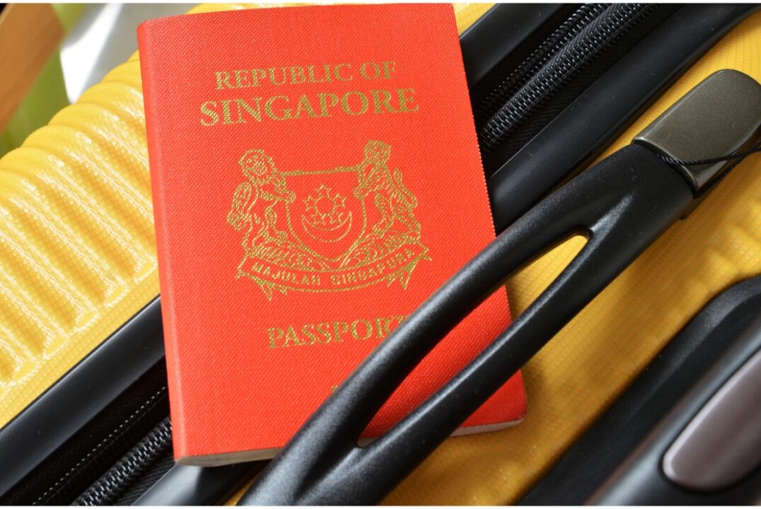 A red Singapore passport tucked into the handle of a yellow-and-black suitcase.