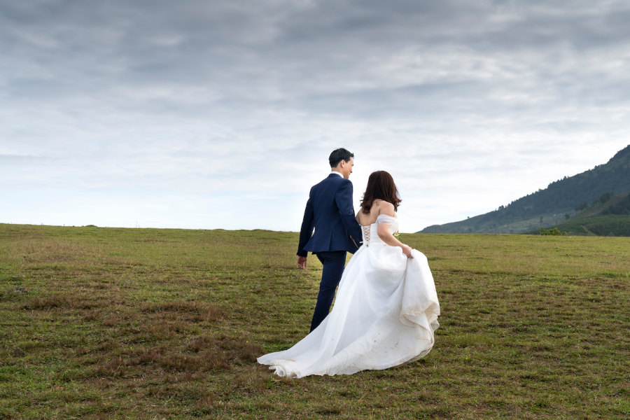 bride and groom walking on a hill with grey clouds above
