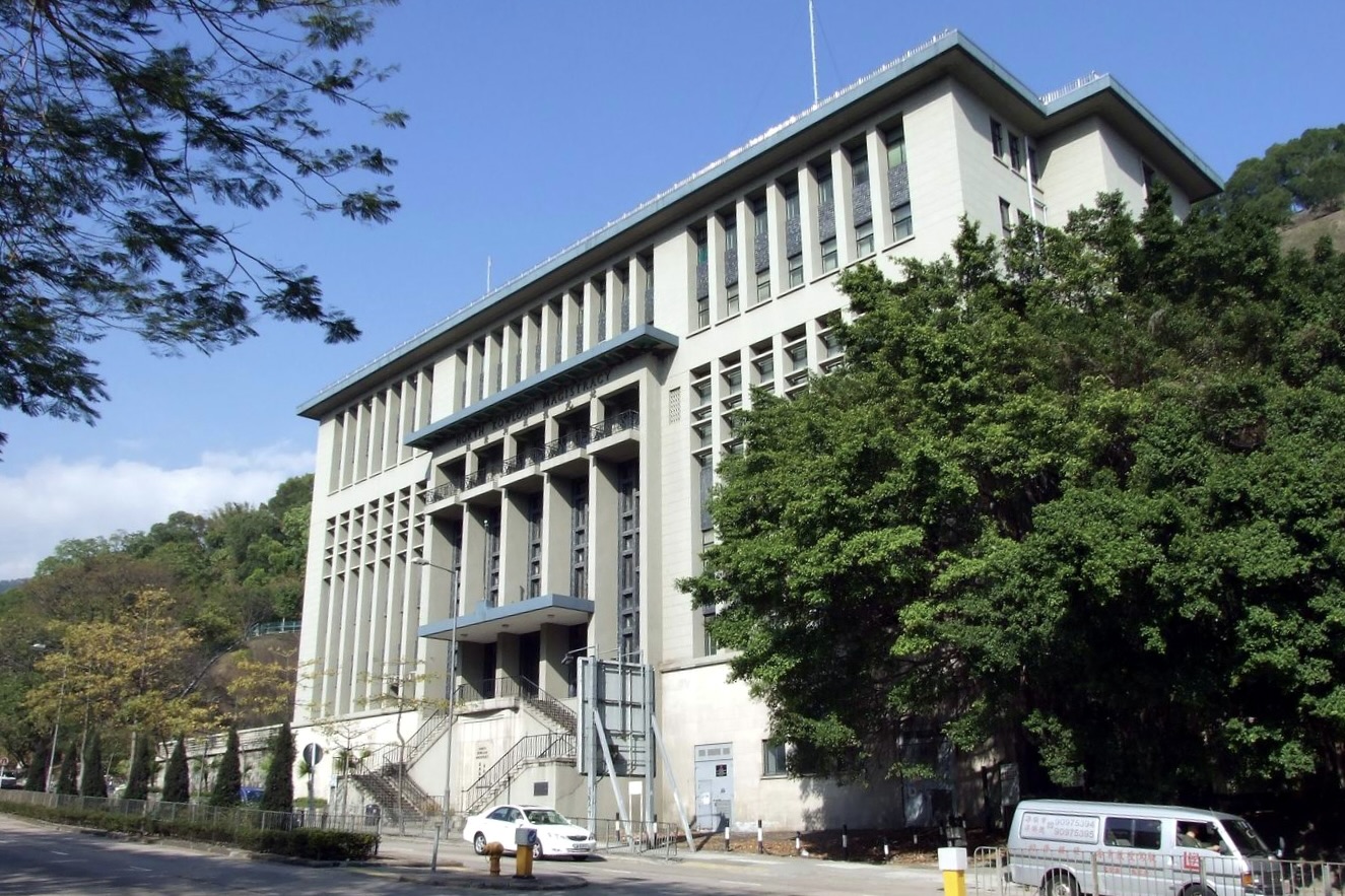 The facade of the Former North Kowloon Magistracy Building has tall narrow windows that face the main road. There are two staircases that lead up to the main entrance.