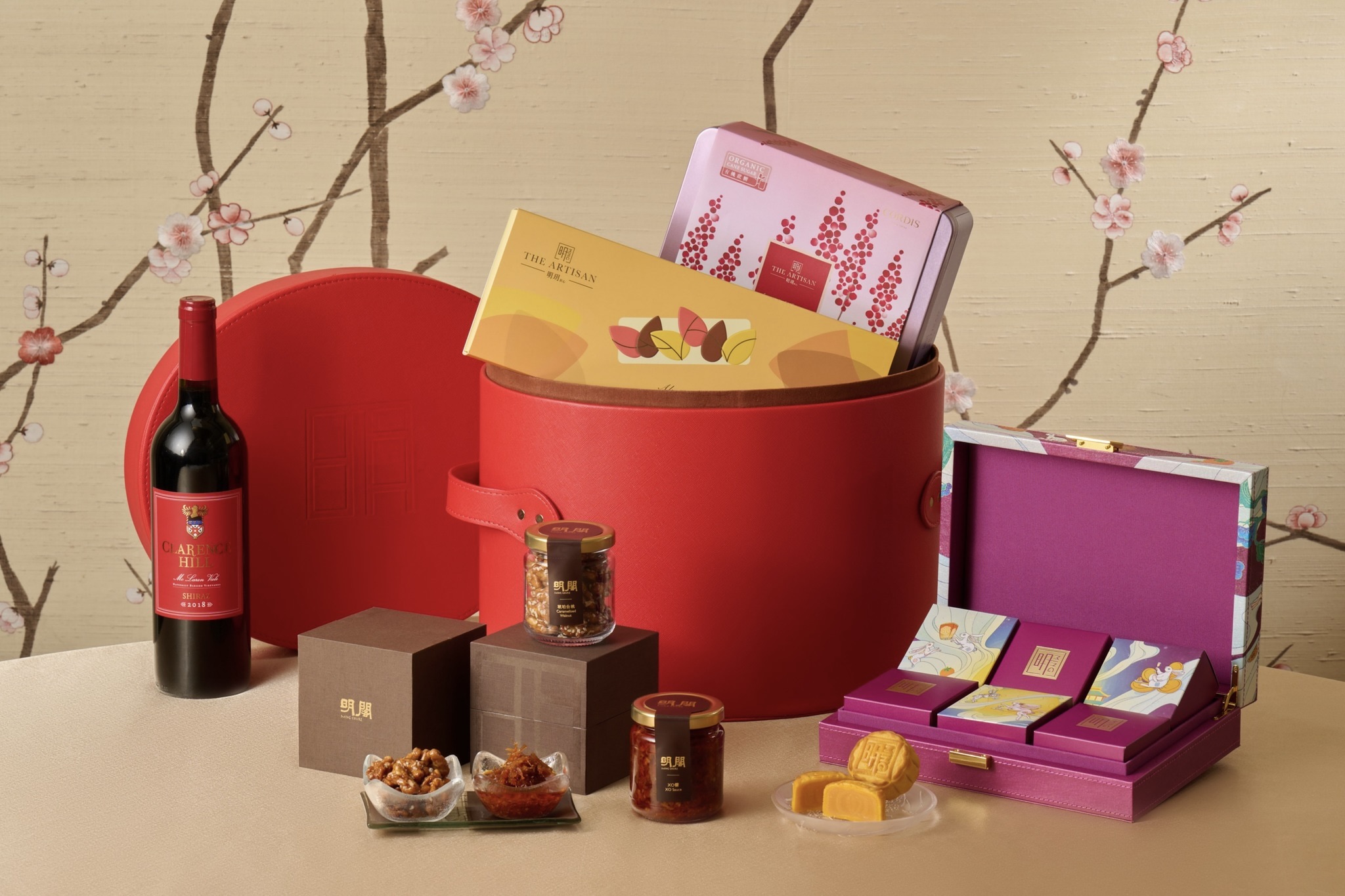 A festive mooncake hamper from Cordis with wine, caramelised walnuts, XO sauce, and mooncakes. The contents of the hamper come in a red cylindrical box containing square boxes with the nuts and sauce. There are other boxes that contain the mooncakes.