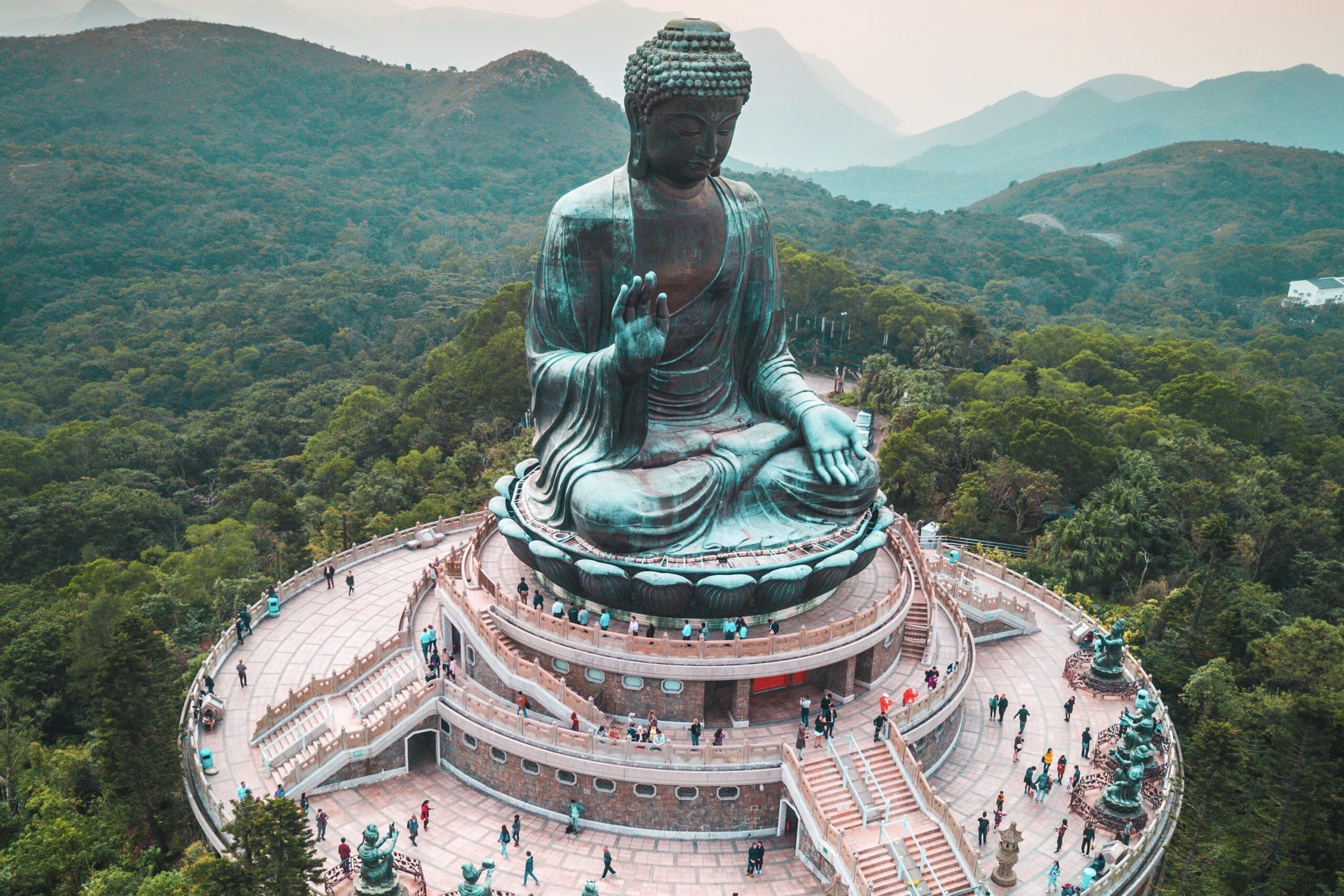 A bird's-eye view of the Tian Tan Buddha. The crowds around the base of the statue can be seen, as well as the forested hills that surround the statue.