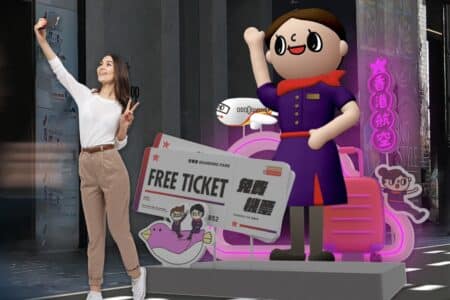Hong Kong Airlines Will Distribute 1,000 Free Tickets At Fashion Walk On August 26 & 27 A woman holds up her mobile phone to take a selfie in front of a Hong Kong Airlines installation to promote a free ticket giveaway.