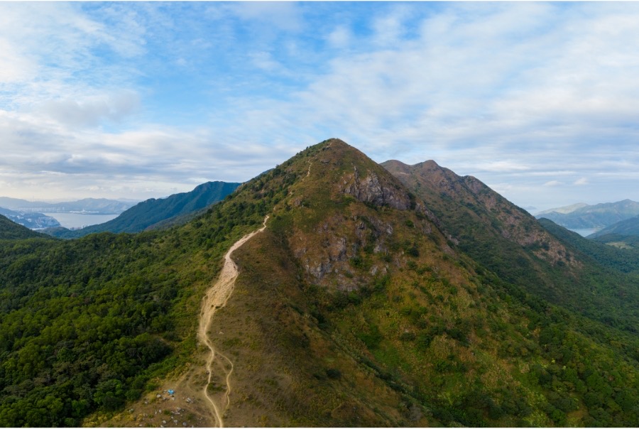 Pyramid Hill in Ma On Shan Country Park in Hong Kong. There is a trail running up one side of the hill. In the background, between other hills, you can glimpse the see and a township.