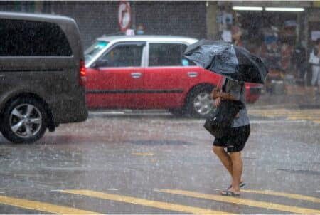 Typhoon Saola: Hong Kong Observatory To Issue T3 Signal On Thursday Evening A woman walks in heavy rain with an umbrella. There are cars, most notably, a red Hong Kong taxi, in the background.