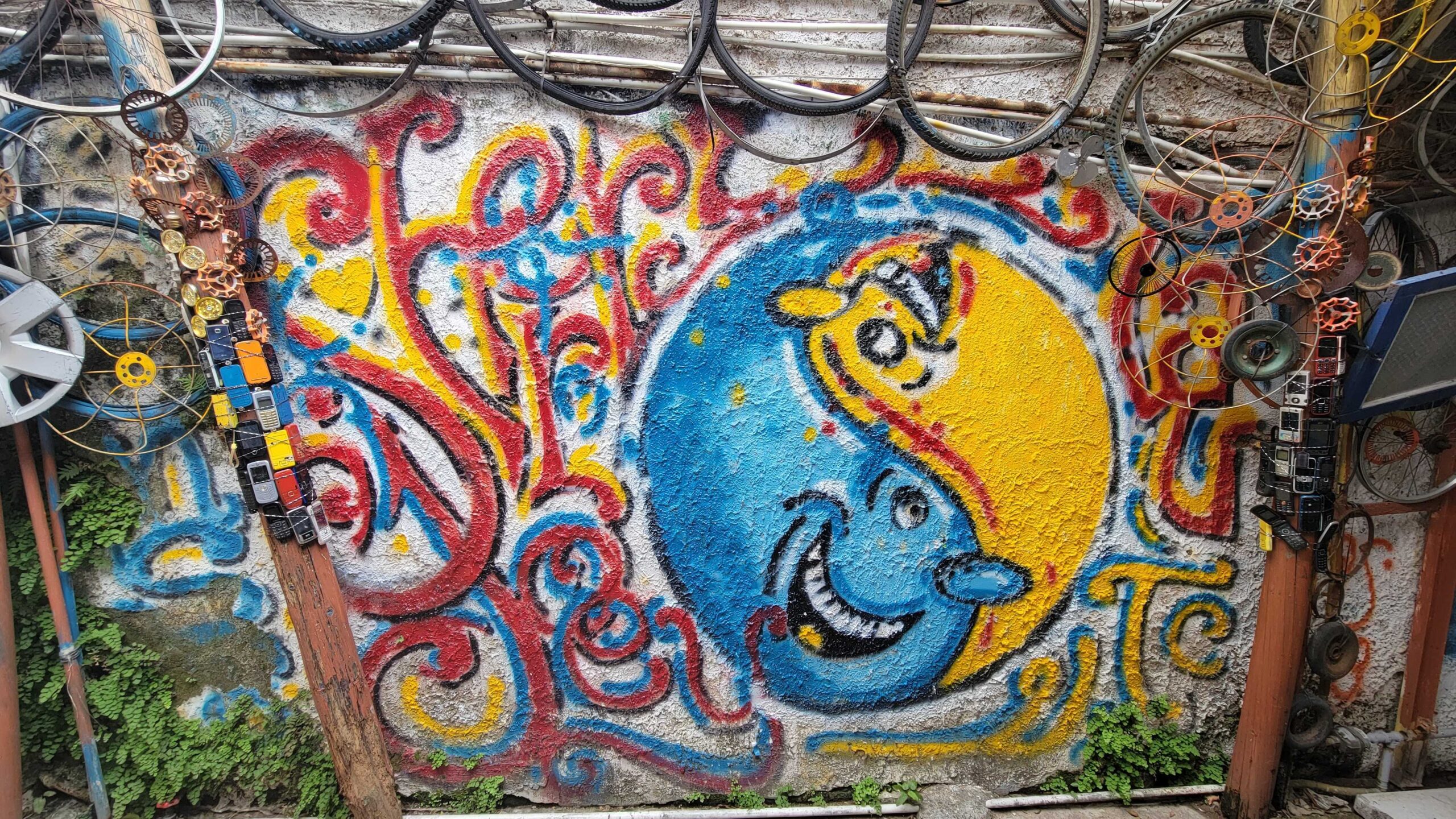 A yin-yang depiction on a wall of a former leather factory in Peng Chau. It is surrounded by odds and ends like bicycle tyres, old cellphones, and gears.