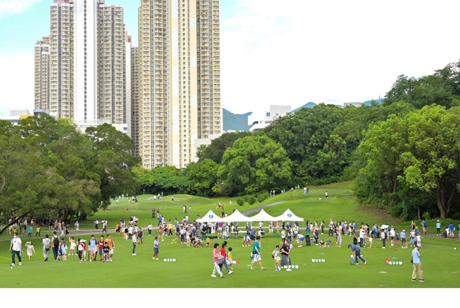 A view of the Hong Kong Golf Course at Fanling. People are walking on the lawns, which also has tents. There is a block of high-rise apartments overlooking the golf course.