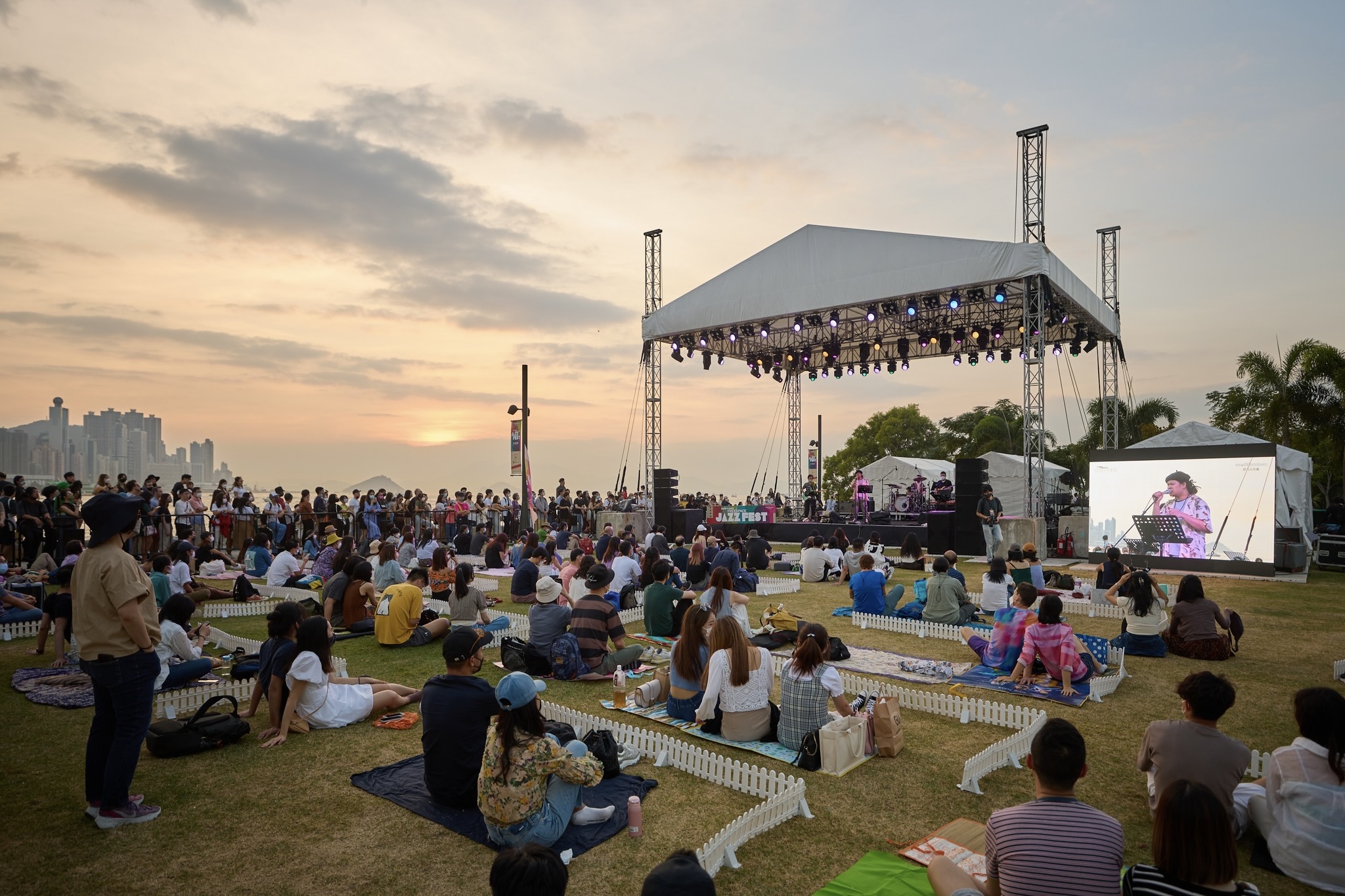 people sit outdoors on a lawn and listen to a music performance