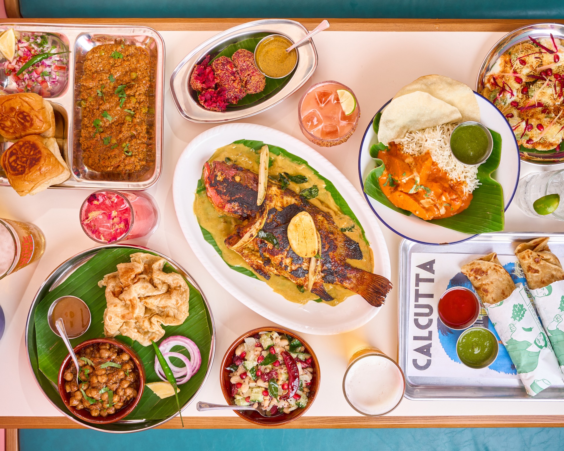 an overhead view of the offerings from bengal brothers, which includes keema pav, a whole fish, butter chicken, and kati rolls.