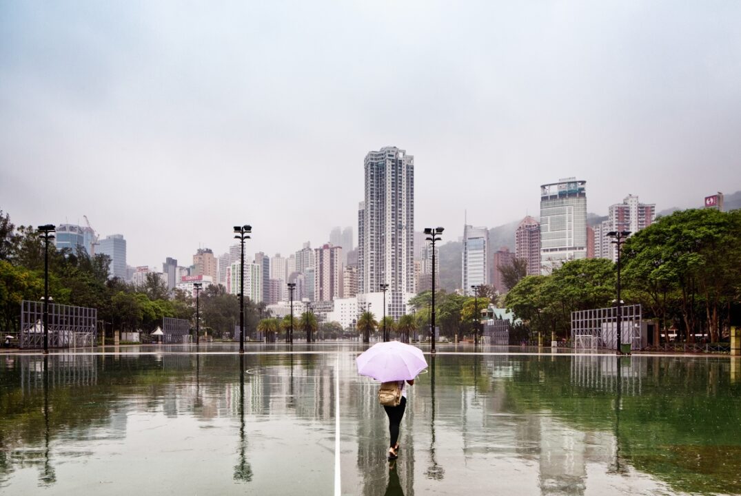 a woman holding an umbrella walks through a rain-soaked football pitch in hong kong