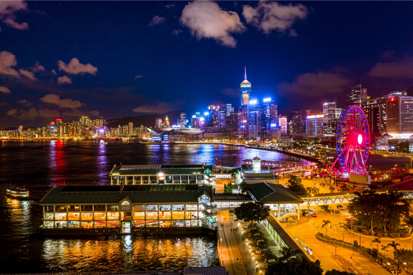 An overhead view of the star ferry pier at central and the neighbouring central pier 8. the hong kong observation wheel is on the right and the skyline of eastern hong kong island is in the background.