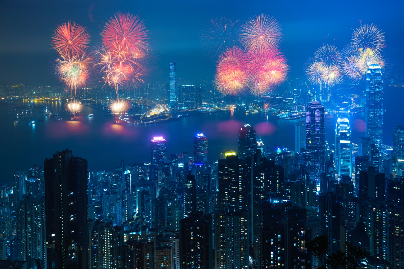 a view of the fireworks in hong kong from the peak. the hong kong island skyscrapers are in the foreground and the kowloon skyline is in the background.