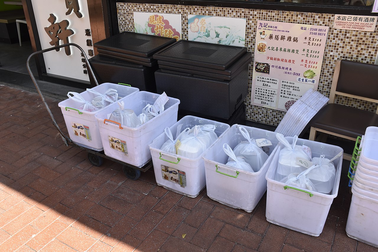 White containers lined up on a Hong Kong pavement with plastic bags containing takeaway orders from a restaurant.