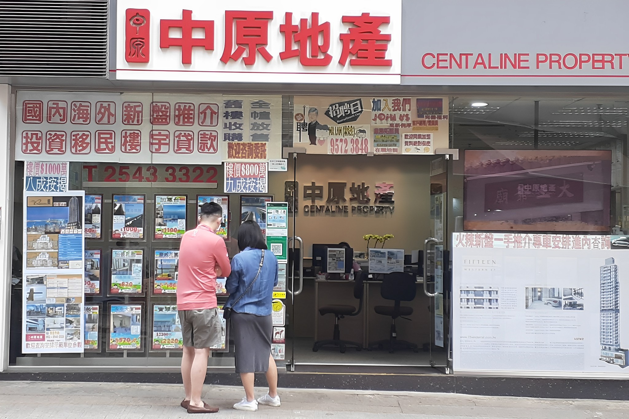 a man and woman stand outside a real estate in hong kong and reas the listings